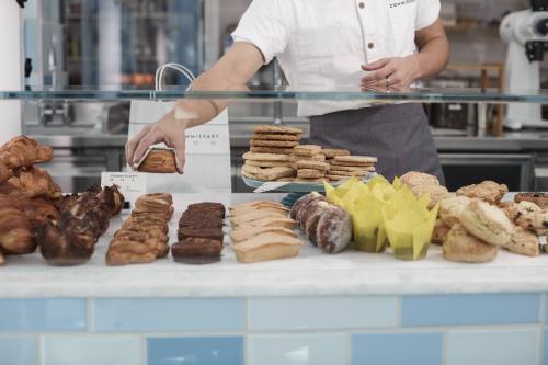 a baker reaches into a pastry shelf to grab a baked good