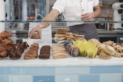 a baker reaches into a pastry shelf to grab a baked good