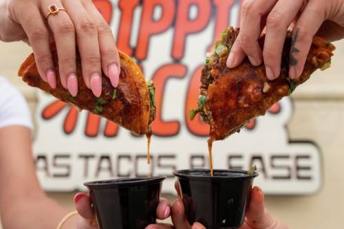 hands hold tacos dipped in sauce