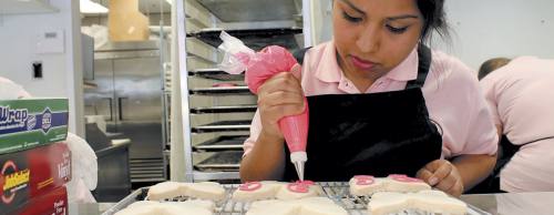 Decorator Alexis Lozoria decorates butterfly-shaped cookies with pink icing.