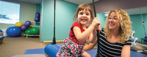 Angela Ullman, a physical therapist at Little Tesoros Therapy Services in Cedar Park, works with 3-year-old Sonia Mann on a bolster swing to help improve body strength and body awareness.