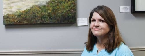 Lauren Combs, president of The Woodlands Art League, stands in front of one of her paintings hanging in the South Montgomery County Community Center. n