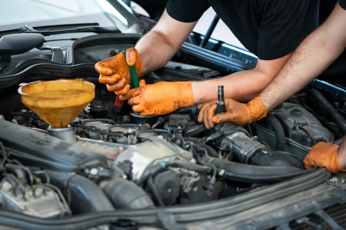 Two mechanics working on a vehicle in a garage or service workshop, close up of their gloved hands and equipment in the engine compartment