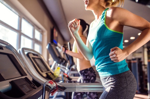 Two attractive fit women running in sports clothes on treadmills in modern gym