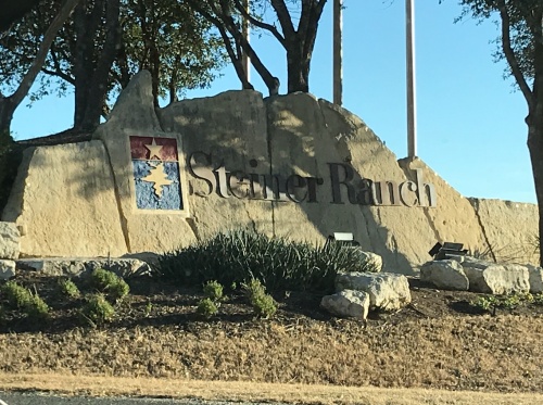 A painted stone entrance sign to Steiner Ranch is partially covered in a late afternoon tree shadow. 