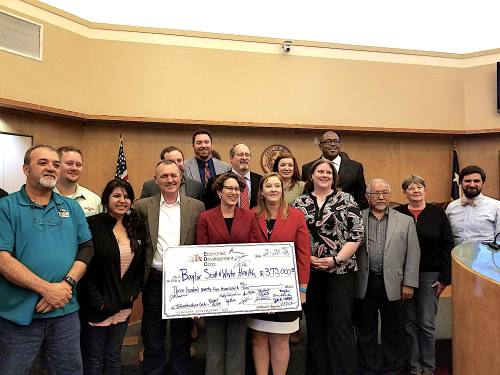 Buda City Council, staff and the Buda Economic Development Corps. stand with sign check to Baylor Scott & White. 