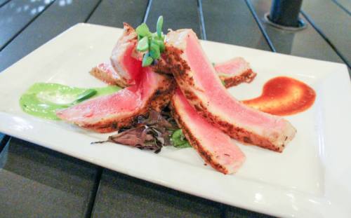 Wild-caught tuna is cooked rare and blackened, garnished with Sriracha sauce and wasabi sauce and served with one side and a salad.