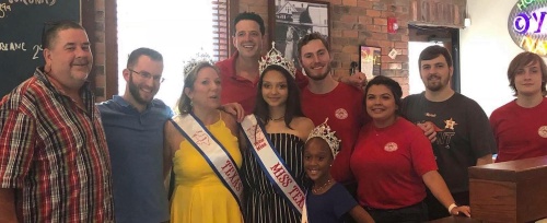 Antonio Moreno (back, center in red) poses with Andrew Leaper (left), Brian Walz (second from left in blue) staff, pageant winners and one of the children who has benefited from the Snowdrop Foundation, Fish City Grill's chosen charity for the event. 