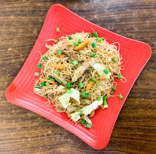 This traditional Filipino noodle dish includes white rice noodles with chicken, soy sauce, green cabbage, carrots, onions and garlic topped with green onions.