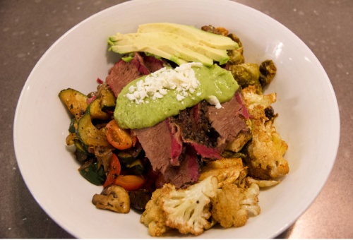 A brisket bowl comes with cauliflower, mushrooms, mixed veggies, avocados, tomatoes, Brussels sprouts and an avocado verde sauce.